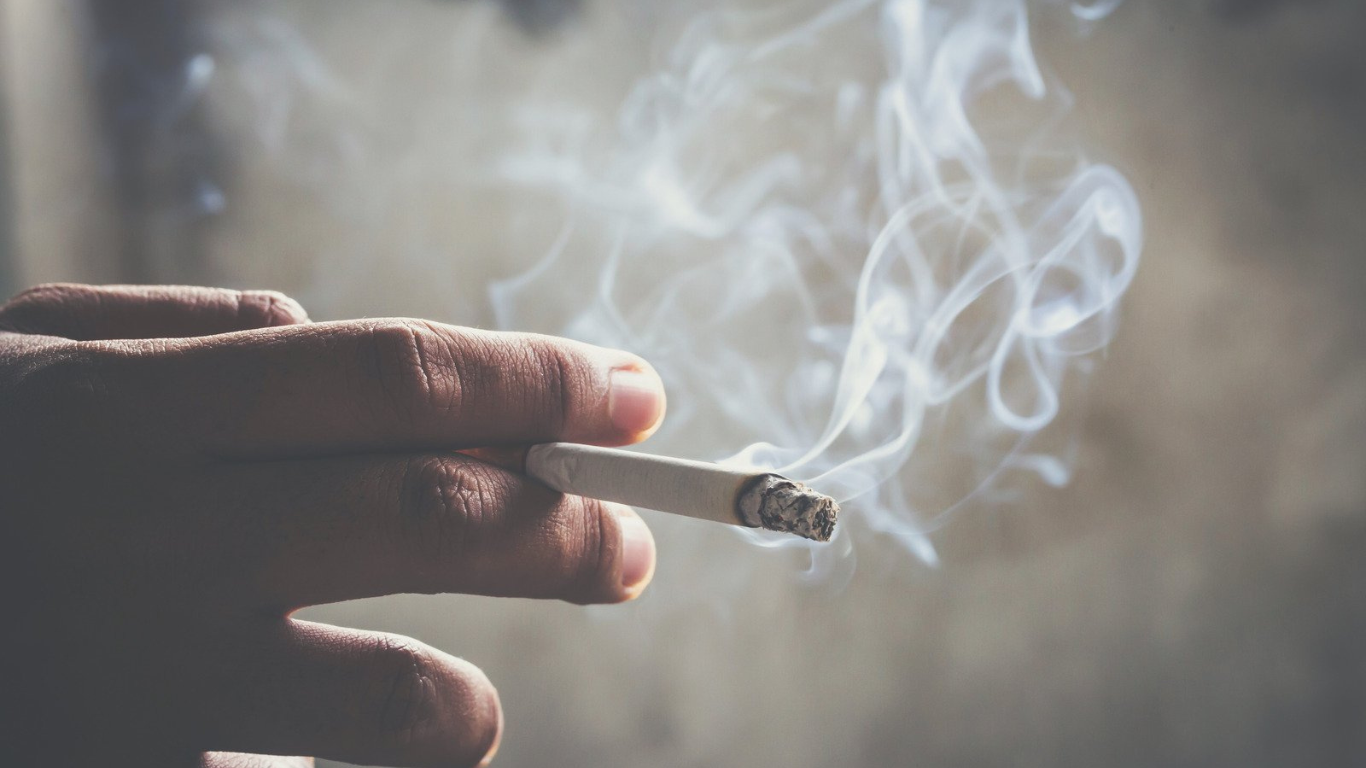 Why That Tobacco Stench Still Lingers (And How to Truly Remove It) Hand holding a lit cigarette with smoke causing strong tobacco stench.