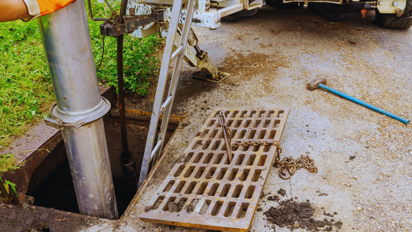 Can Raw Sewage Cleanup Help Save Your Belongings Close-up of a worker lifting a sewer grate with a wrench, addressing raw sewage cleanup as part of emergency restoration.